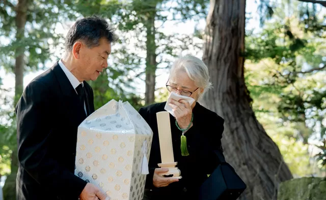 遺骨と白木の位牌を持ちながら故人を偲ぶ高齢の男女